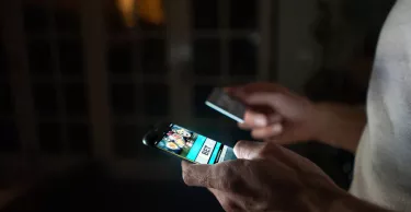 Close-up on a person betting online at home on their cell phone using their credit card.