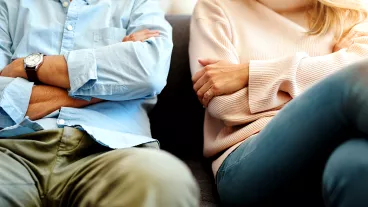 Close up of divorcing man and woman sitting on a sofa with their arms crossed.