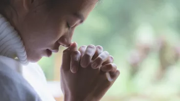 A woman with clasped hands praying.